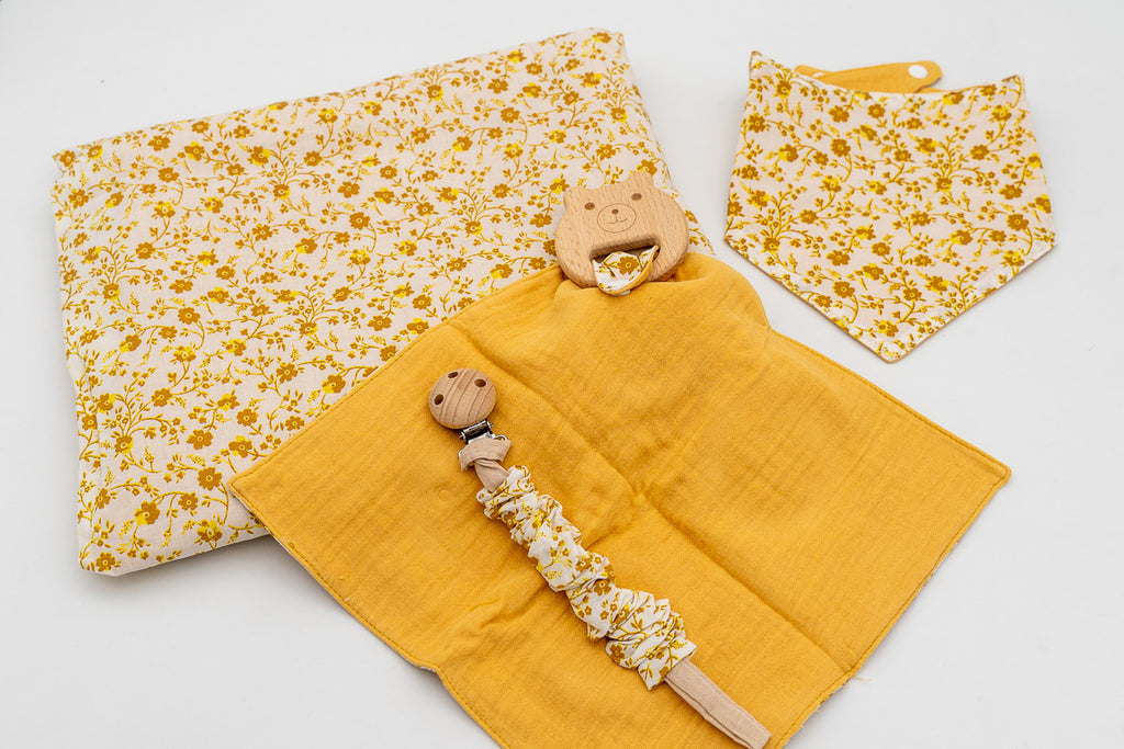 Conjunto mostarda com manta de flores, babete bandana, fralda de musselina mostarda com mordedor de madeira em forma de ursinho e prende-chupetas com mola de madeira.