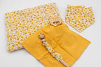Conjunto mostarda com manta de flores, babete bandana, fralda de musselina mostarda com mordedor de madeira em forma de ursinho e prende-chupetas com mola de madeira.