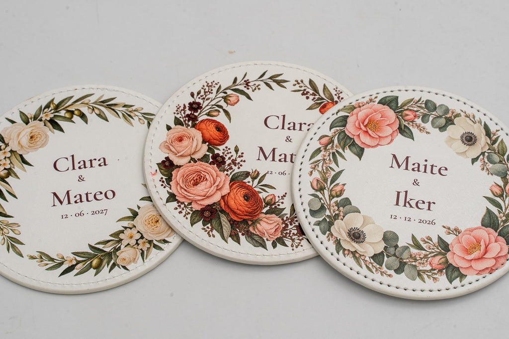 Três bases para copos redondas brancas com flores a cores e nomes dos noivos.