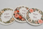 Três bases para copos redondas brancas com flores a cores e nomes dos noivos.