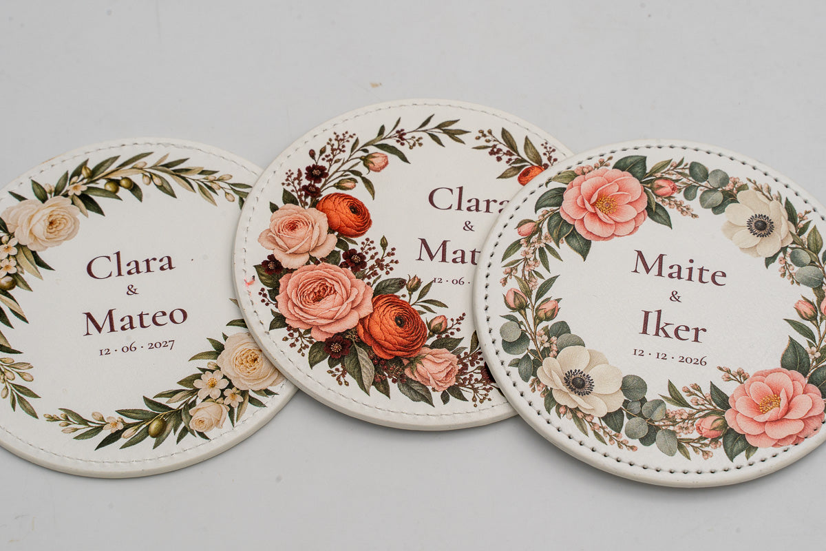 Três bases para copos redondas brancas com flores a cores e nomes dos noivos.