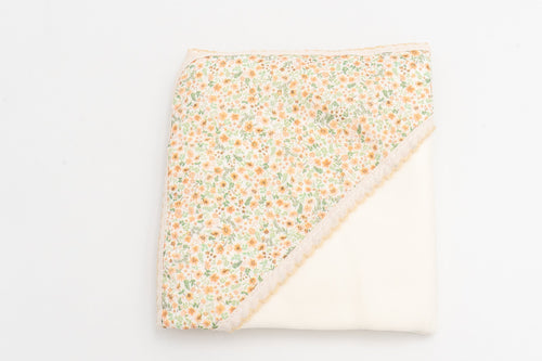 Manta para bebé mostarda dobrada, com o capuz estampado de flores e a renda a condizer.