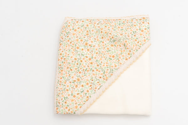 Manta para bebé mostarda dobrada, com o capuz estampado de flores e a renda a condizer.