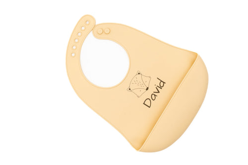 Babete de silicone bege com nome e motivo animal geométrico, visto na diagonal.