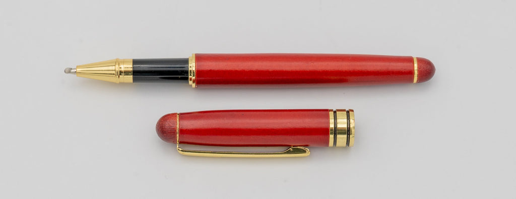 Caneta de madeira de acabamento avermelhado com tampa retirada e detalhes dourados.