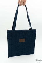 Bolso vaquero tipo tote sostenido por la mano con parche central que indica Fashion Bag.