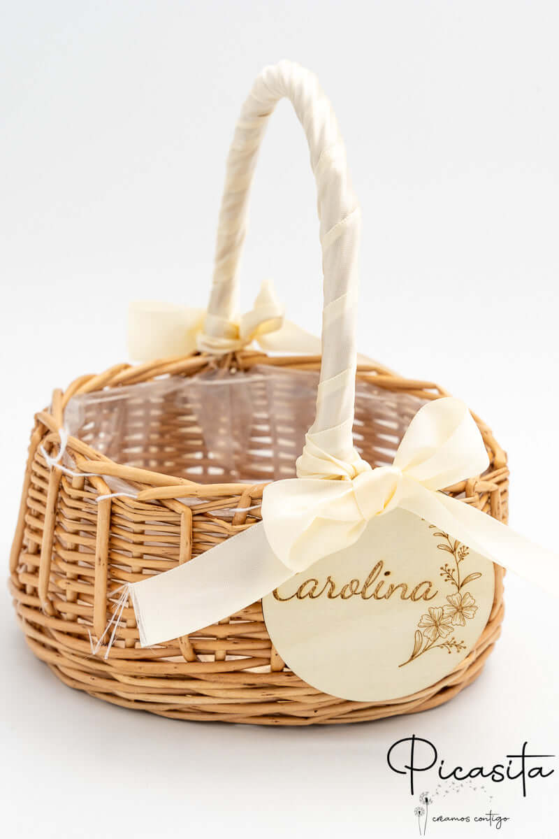 Cestito de ratán con lazo de raso crema y medalla de madera con nombre grabado.