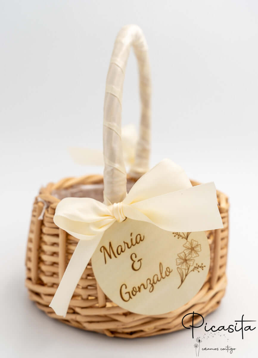 Cesto de ratán con asa envuelta en lazo crema y disco de madera con nombres de los novios.