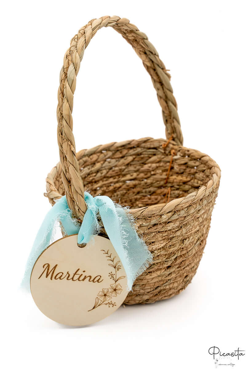 Cesta de mimbre con asa trenzada, lazo azul deshilachado estilo boho y disco de madera.