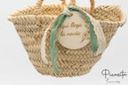 Cesto de hoja de palma con lazo verde y disco de madera decorativo para ceremonia.