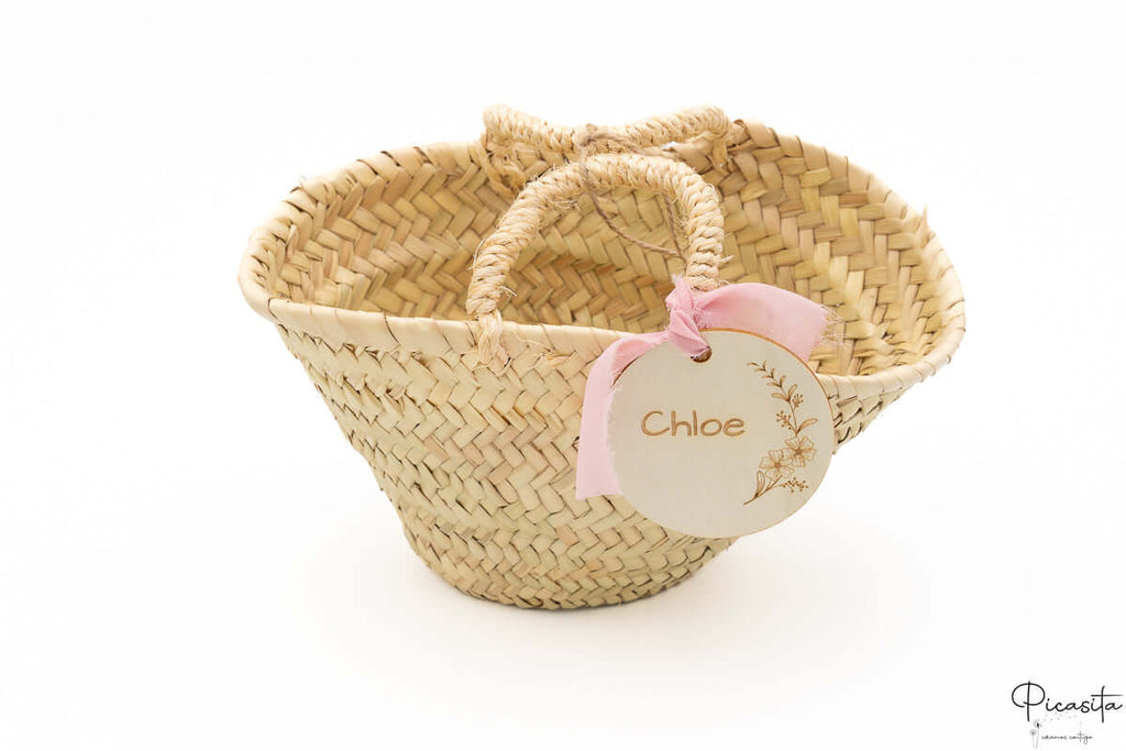 Cesto de fibras naturales con doble asa y lazo de tela color rosa suave.