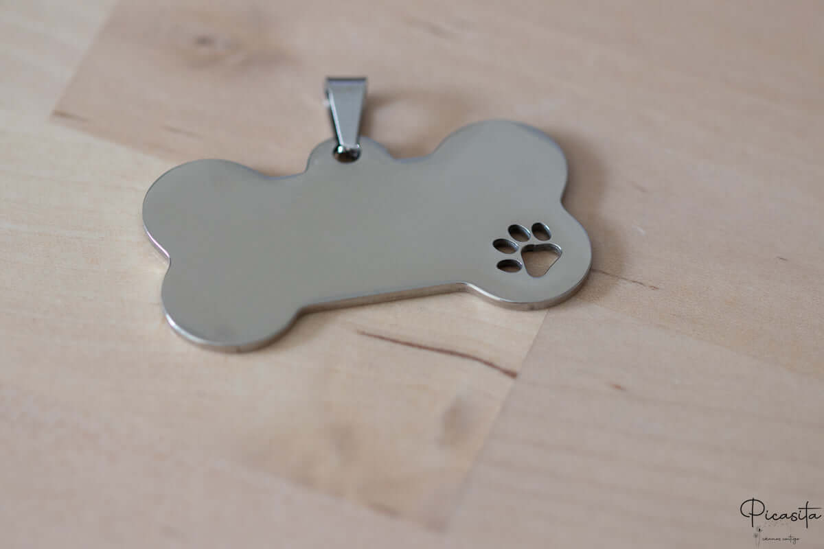Placa identificativa de acero pulido con detalle de pata calada y anilla de sujeción metálica.