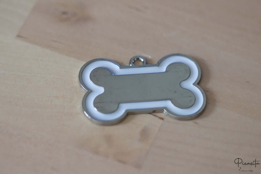 Chapa para perro de acero inoxidable con forma de hueso, centro plateado y borde blanco.
