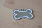 Chapa para perro de acero inoxidable con forma de hueso, centro plateado y borde blanco.