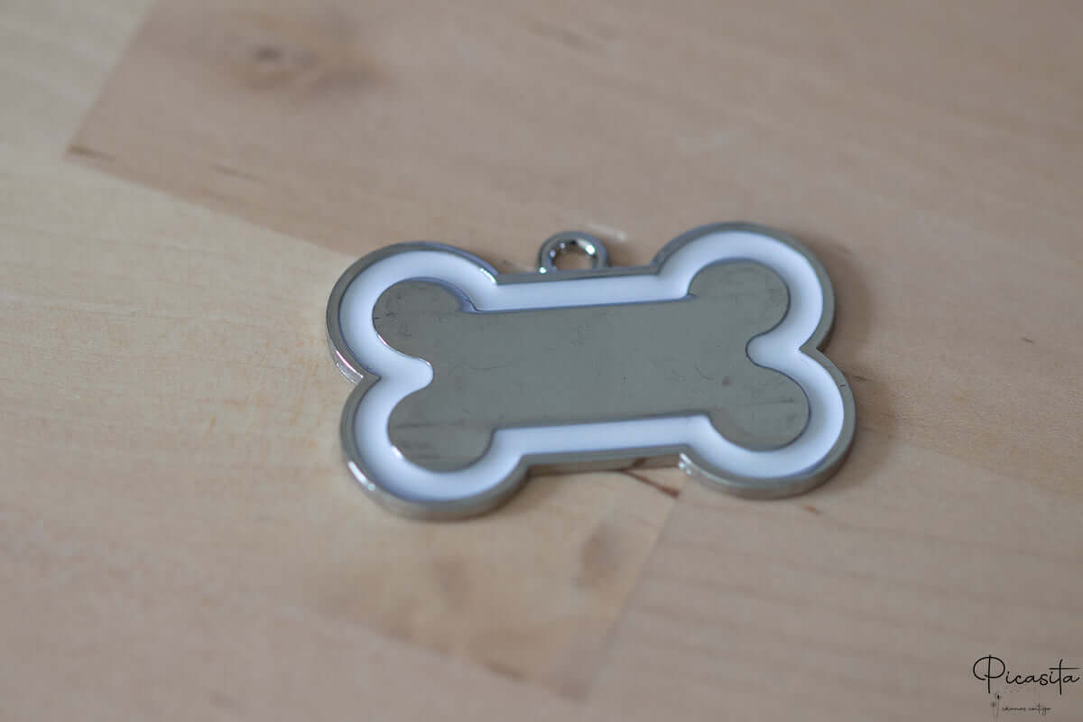 Chapa para perro de acero inoxidable con forma de hueso, centro plateado y borde blanco.