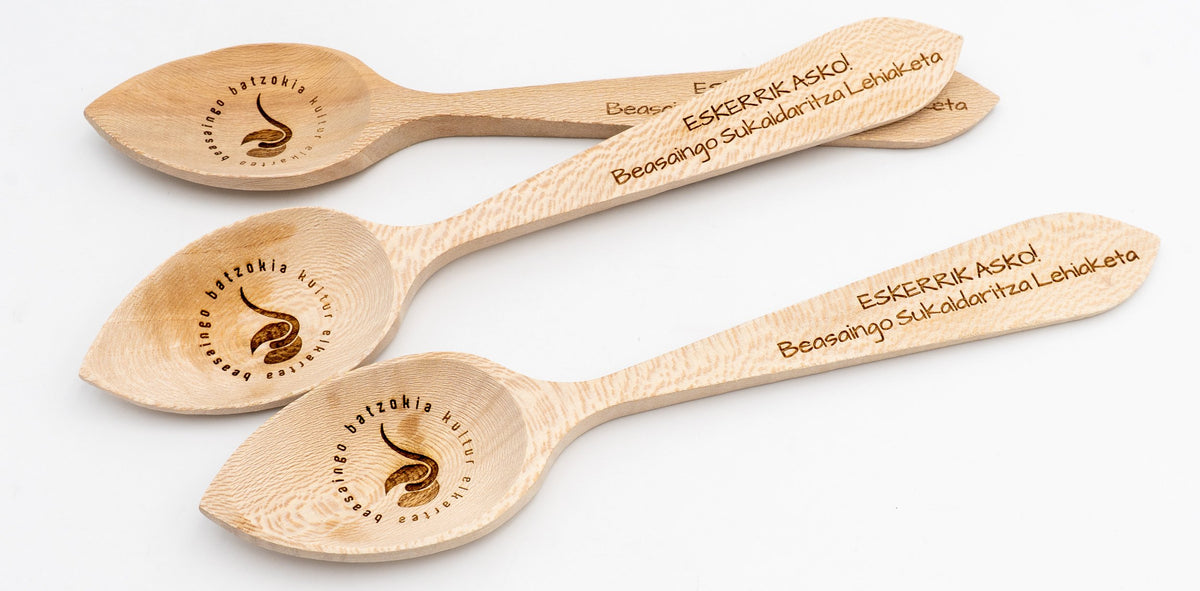 Tres cucharas de madera grabadas con mensajes de agradecimiento y logotipos de concursos culinarios.