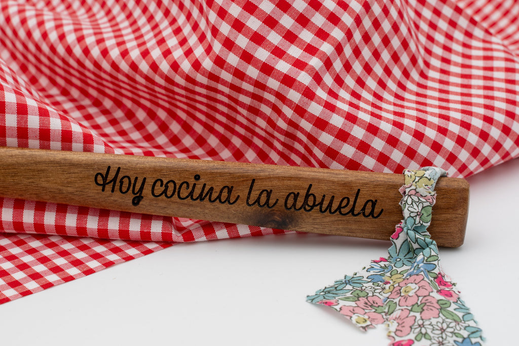 Primer plano de mango de madera con grabado Hoy cocina la abuela y cinta textil floral.