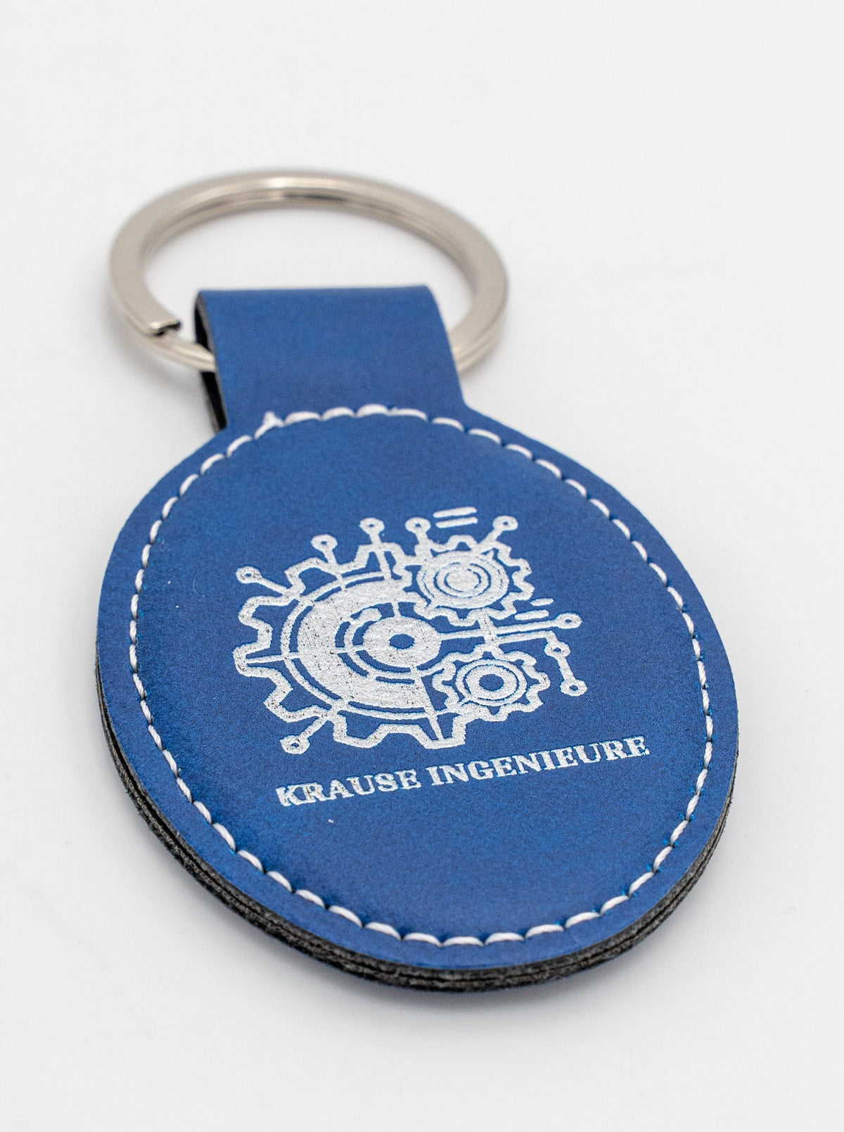 Porta-chaves oval azul com logótipo claro e costura branca.