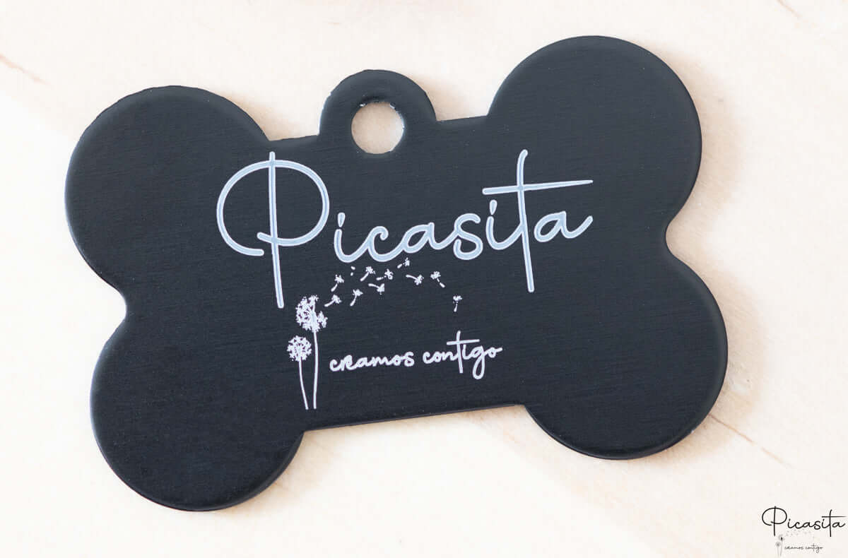 Placa de identificación negra en forma de hueso con grabado láser blanco de nombre y diseño floral.