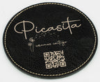 Base para copos redonda preta com marca Picasita e código QR em tom dourado.
