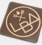 Base para copos quadrada castanha com logótipo de restauração em tom dourado.