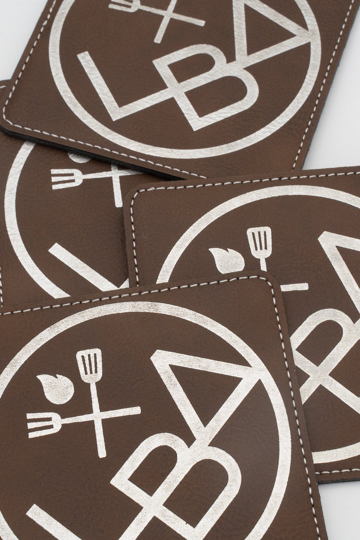 Pormenor de bases para copos quadradas castanhas com logótipo branco e costuras.