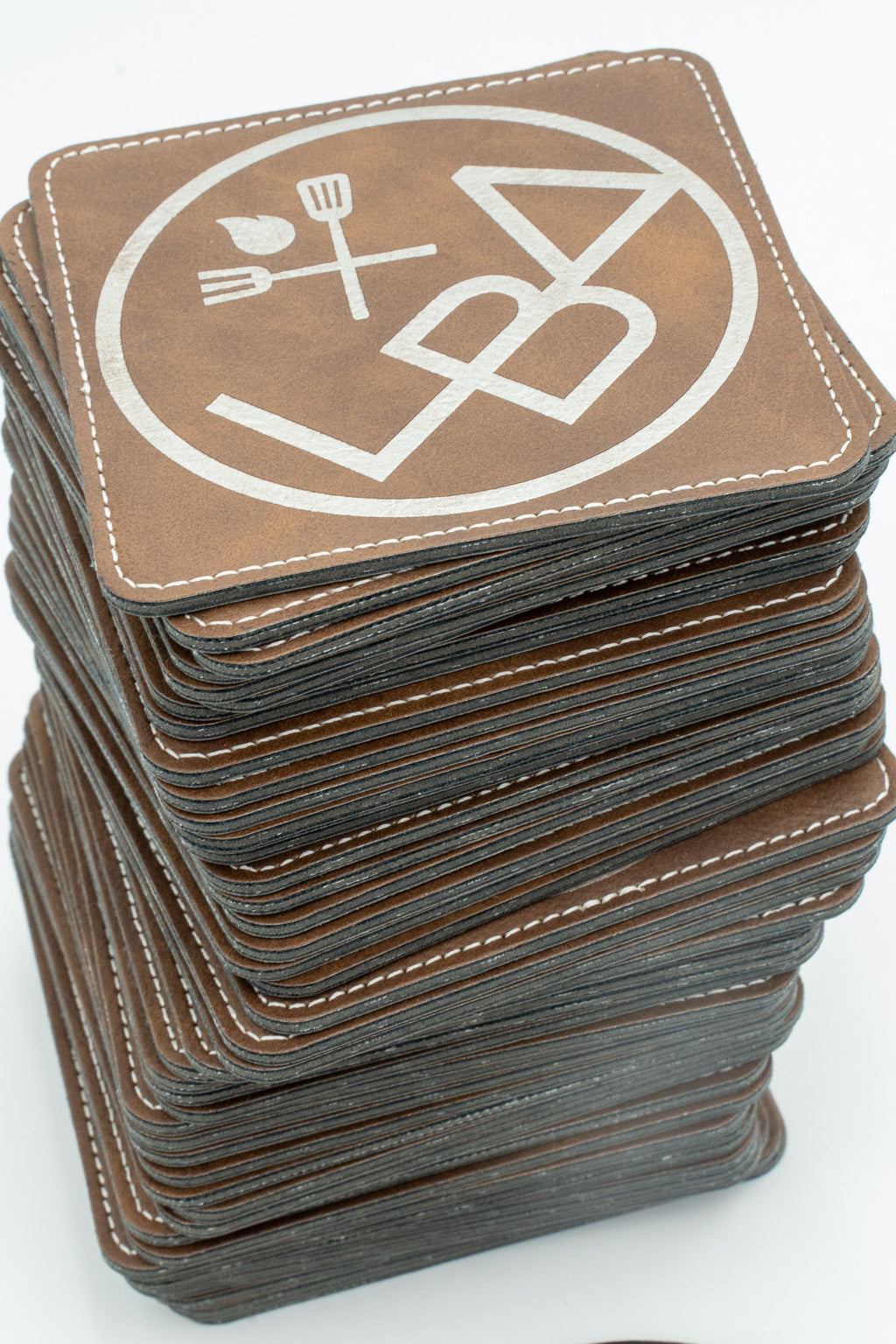 Pilha de bases para copos quadradas castanhas com logótipo branco e costura no contorno.