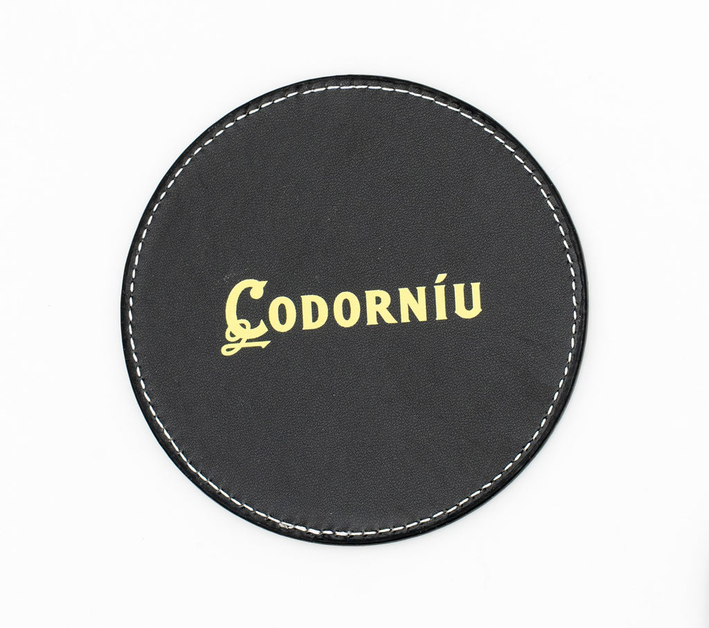 Base para copos redonda preta com logótipo Codorníu em tom dourado.