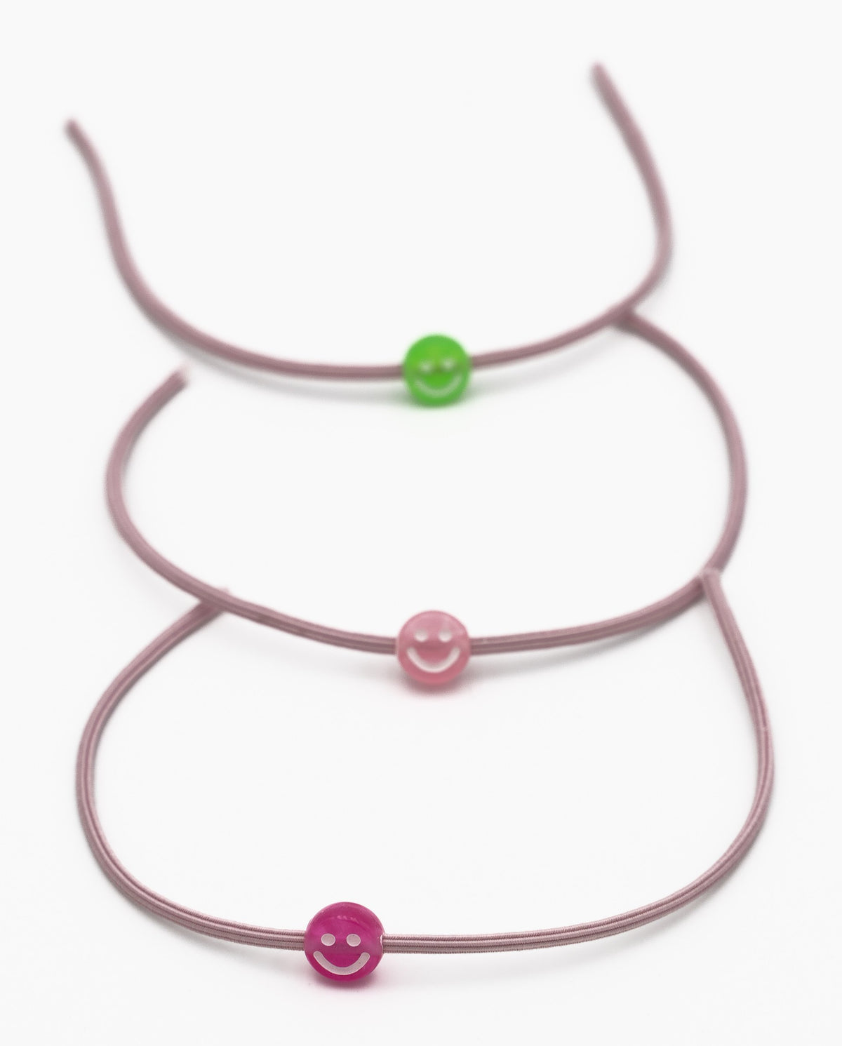 Três pulseiras elásticas malva com contas de silicone em forma de sorriso verde e rosa.
