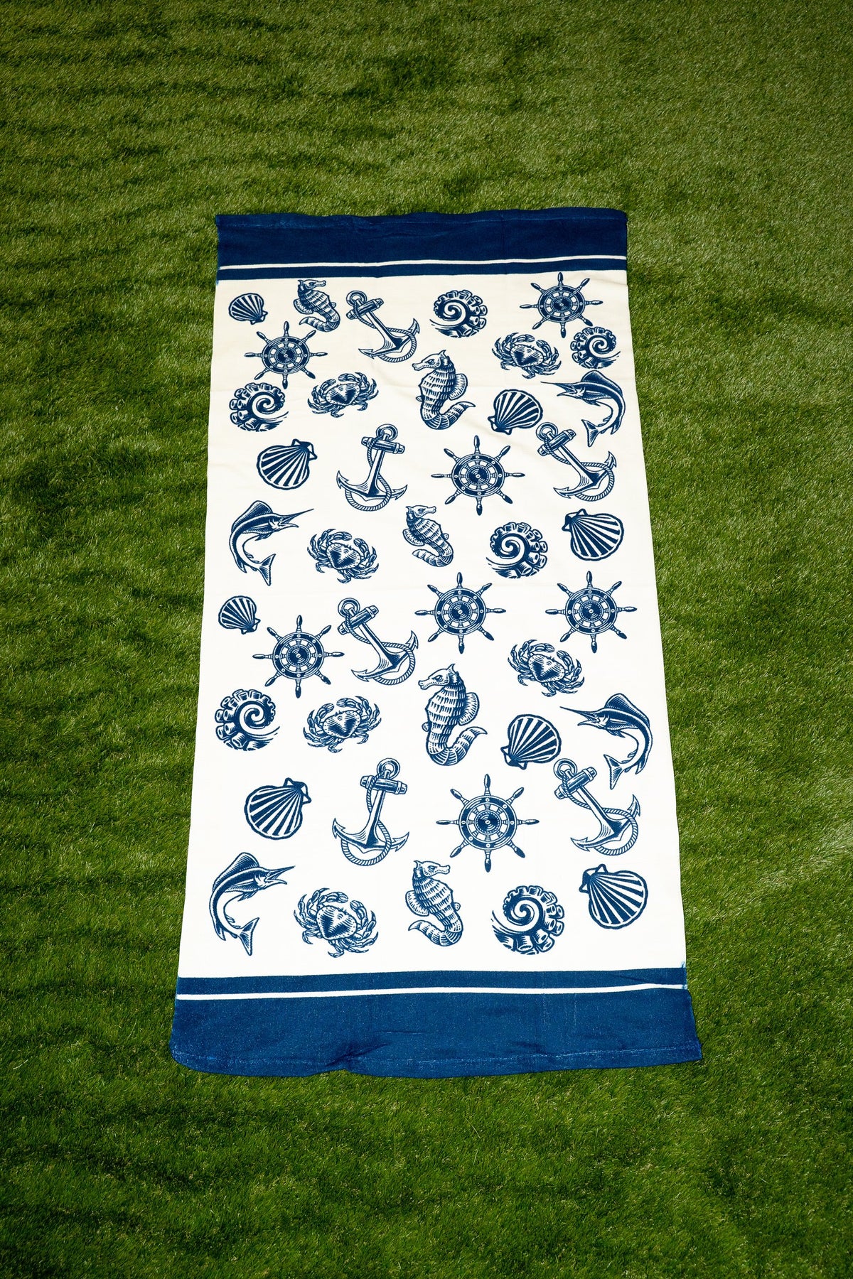 Toalha branca com padrão náutico azul de âncoras, conchas e lemes.