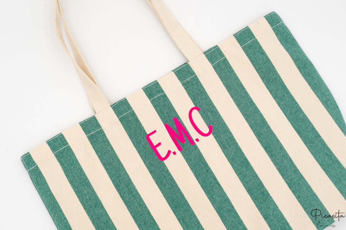 Primer plano de las iniciales personalizadas en color rosa sobre el tejido de rayas verdes.